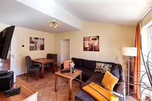 A living room with a sofa, a coffee table, a TV, and a dining area with chairs and a table. - Seepferdchen Vacation Rental – Relaxation in the Coastal Forest, Just 550 m from the Beach - (Koserow)