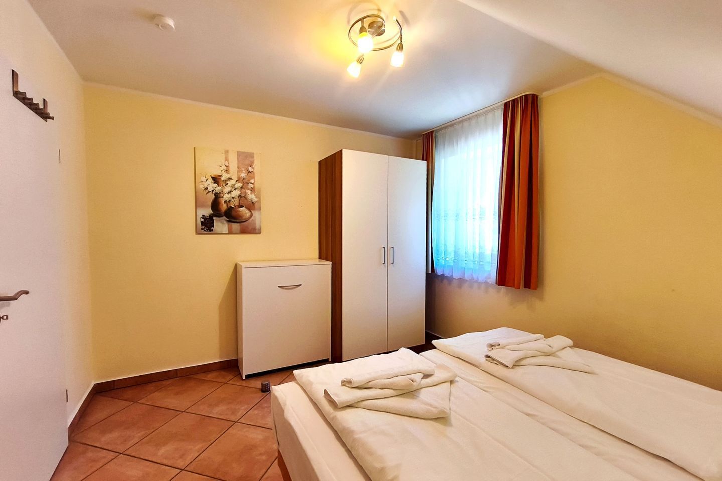 A hotel room with two beds, a wardrobe, a small cabinet, and a painting on the wall.