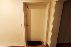 A narrow hallway with a closed door, a doormat, and a light switch on the wall. - Seepferdchen Vacation Rental – Relaxation in the Coastal Forest, Just 550 m from the Beach - (Koserow)