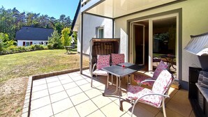 An outdoor patio with a table and chairs, a grill, and a view of a house and trees. - Möwe Vacation Rental – Relaxation Between the Forest and the Baltic Sea - Küstenwaldhaus (Koserow)