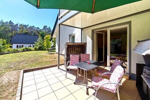An outdoor patio with a table and chairs, a grill, and a view of a house and trees. - Möwe Vacation Rental – Relaxation Between the Forest and the Baltic Sea - Küstenwaldhaus (Koserow)