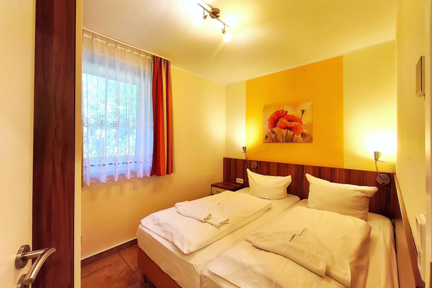 A hotel room with a bed, a window with curtains, a painting on the wall, and a nightstand.