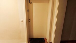 Ein schmaler Flur mit geschlossener Tür, Fußmatte und Lichtschalter an der Wand.