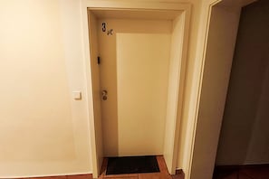 A narrow hallway with a closed door, a doormat, and a light switch on the wall. - Küstenwaldhaus "Muschel" Vacation Rental – Relaxation Between the Forest and the Baltic Sea - (Koserow)