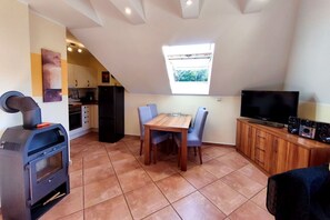 A compact living space with a kitchenette, a dining area with a table and chairs, a TV, and a wood-burning stove. - Küstenwaldhaus "Muschel" Vacation Rental – Relaxation Between the Forest and the Baltic Sea - (Koserow)