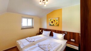 Ein Hotelzimmer mit Doppelbett, Nachttisch, Wandlampe, Fenster und einem Gemälde von Sonnenblumen.
