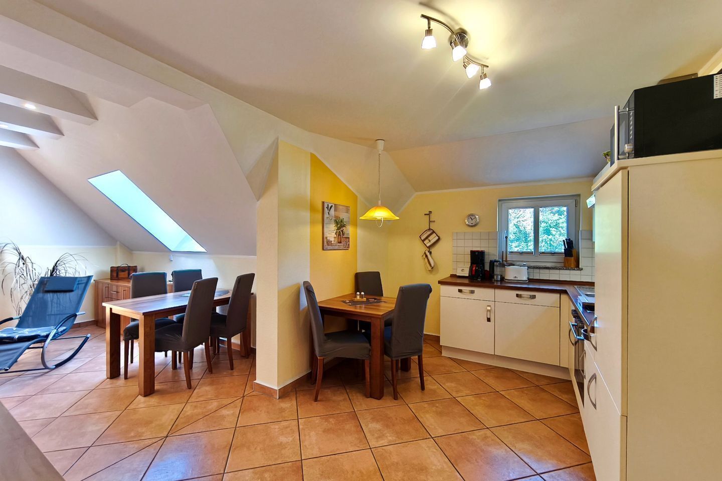 Uma área de refeições com mesa e cadeiras, uma cozinha com janela e um ventilador de teto.