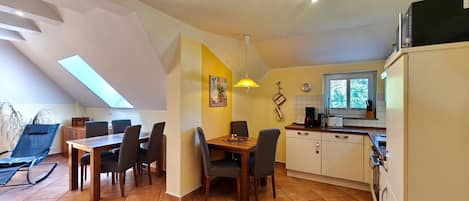 A dining area with a table and chairs, a kitchen with a window, and a ceiling fan.