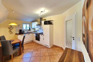 A compact kitchen with white cabinets, a stove, and a sink. There is a dining table with chairs and a pendant light. - Seestern Vacation Rental: Sauna, Fireplace & 550 m to the Baltic Sea Beach - Küstenwaldhaus (Koserow)
