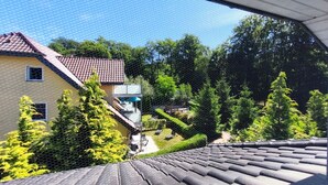 Een woonwijk met een huis, voorzien van een rode pannendak, een balkon en een tuin met diverse planten.