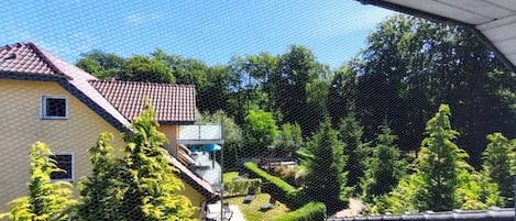 A residential area with a house featuring a red-tiled roof, a balcony, and a garden with various plants.