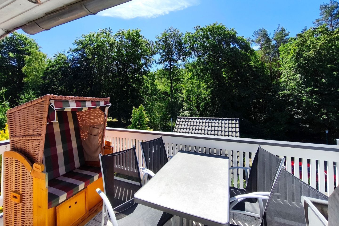 An outdoor patio with wicker furniture, a table, and a view of trees.