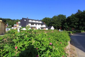 A residential area with a two-story house, a garden with blooming flowers, and a road. - Delfin Vacation Rental – Sauna, Fireplace & Near the Beach - Coastal Forest House (Koserow)