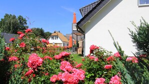 Un jardín con flores rosadas y un edificio blanco con techo inclinado.