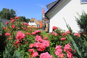 A garden with pink flowers and a white building with a sloped roof. - Delfin Vacation Rental – Sauna, Fireplace & Near the Beach - Coastal Forest House (Koserow)