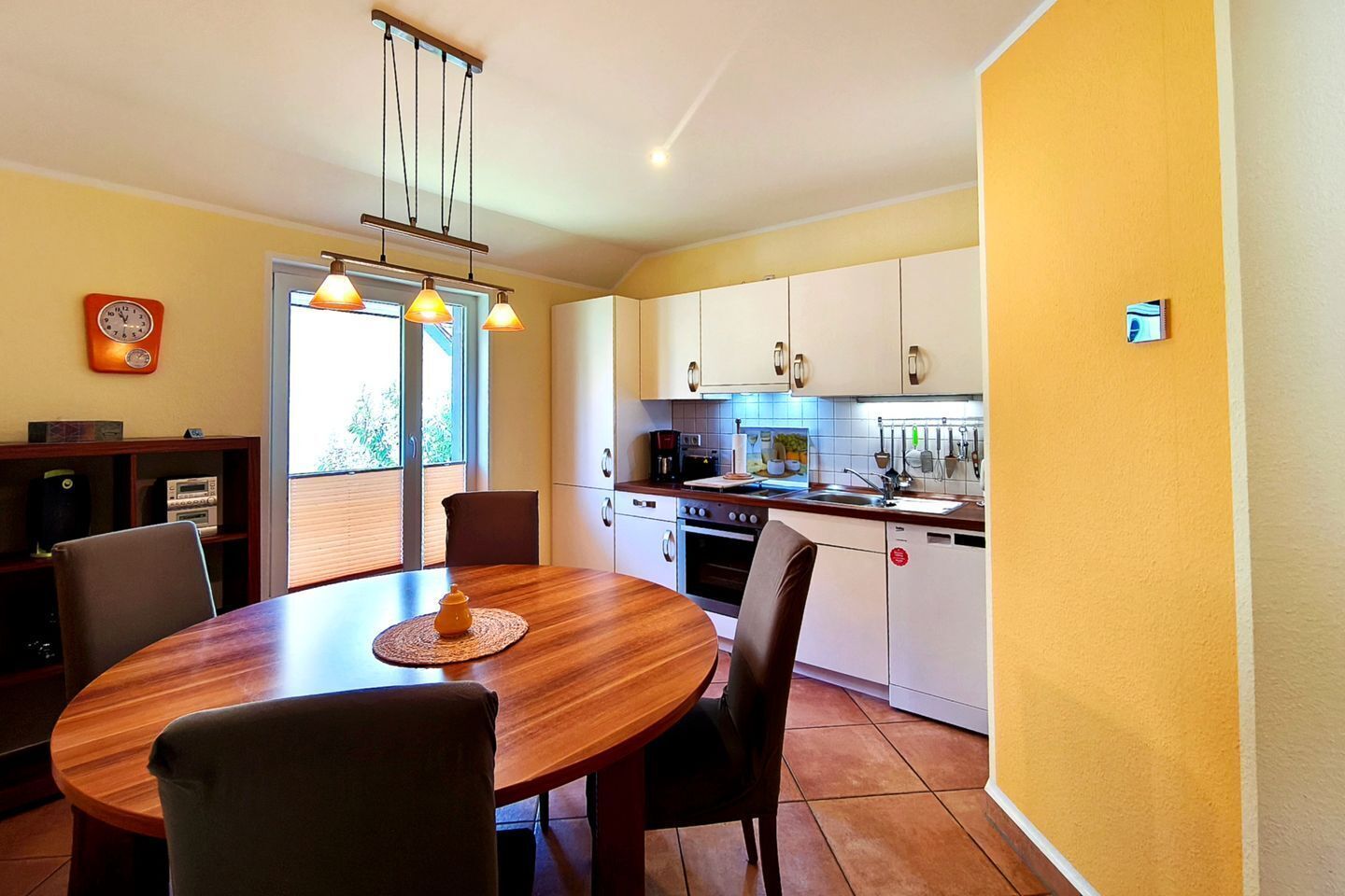 Uma cozinha moderna com armários brancos, uma mesa de jantar com cadeiras e um lustre.