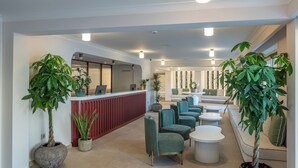 A reception area with a red counter, seating arrangements, and potted plants. - Villa Coo (Kos)