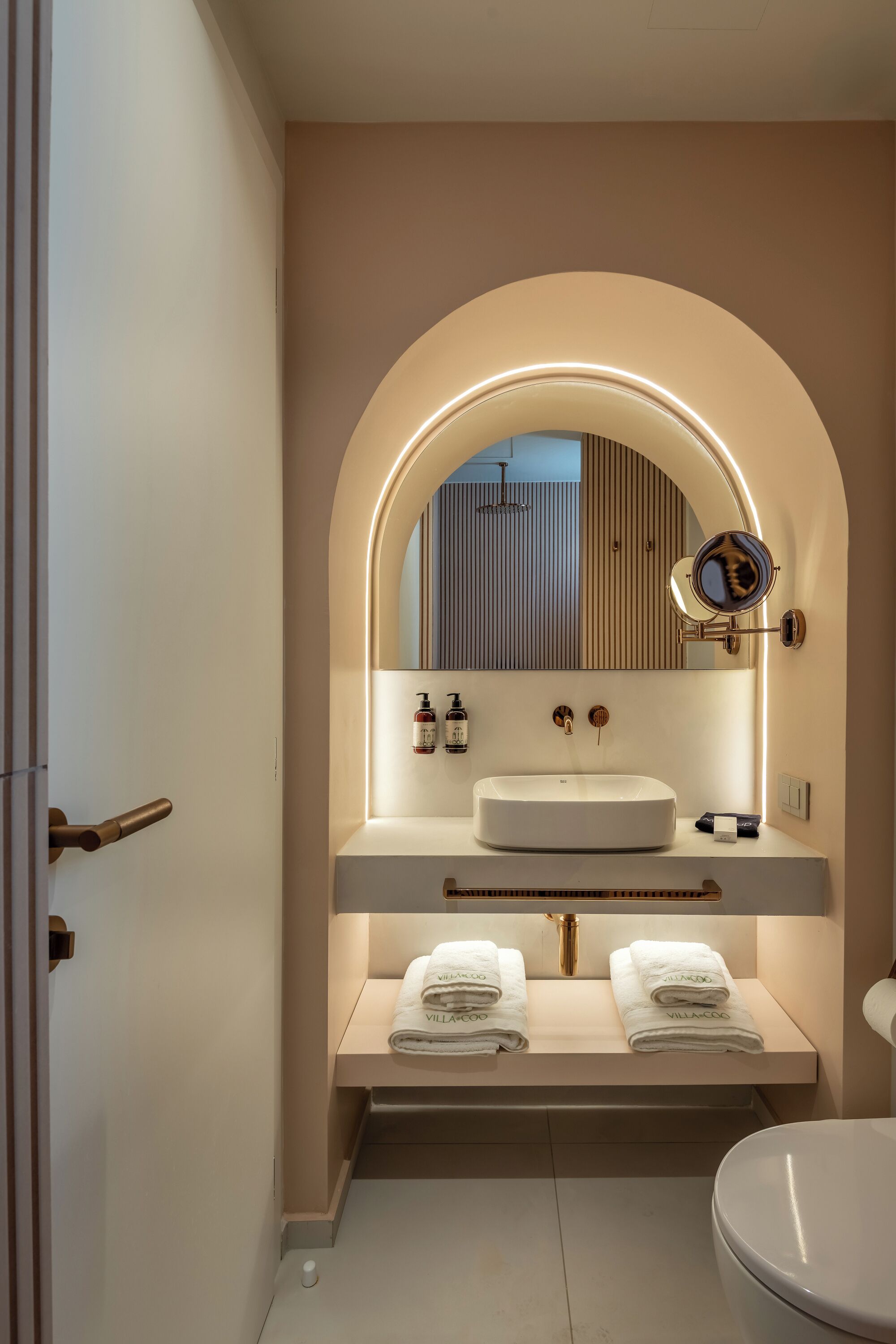 Un baño moderno con un espejo arqueado grande, un lavamanos blanco y dos toalleros.