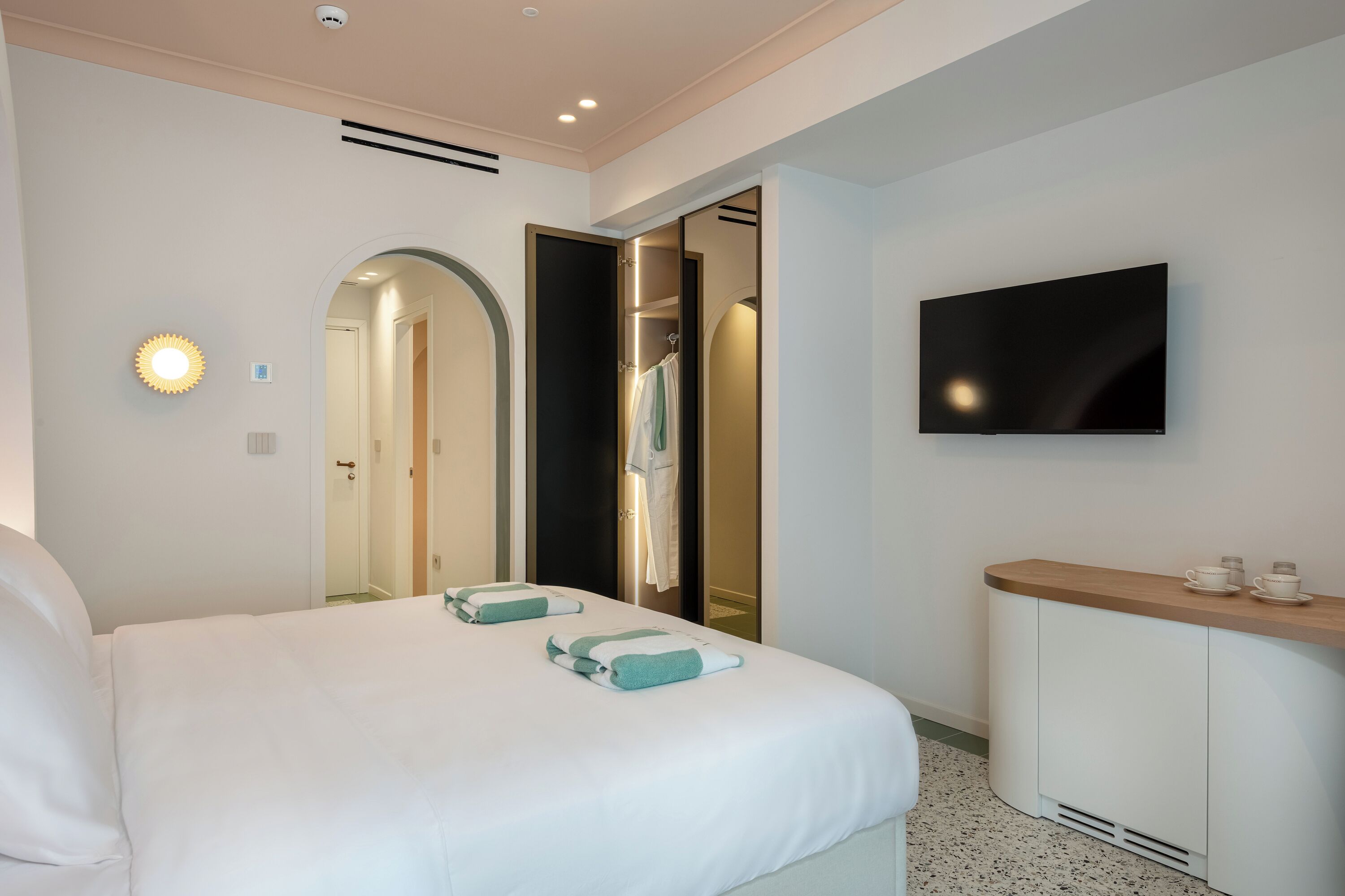 Una habitación de hotel con una cama, un televisor montado en la pared, una tocador con espejo y una puerta que da al baño.