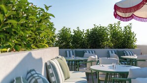 An outdoor seating area with tables and chairs, a striped sofa, and a decorative umbrella. - Villa Coo (Kos)