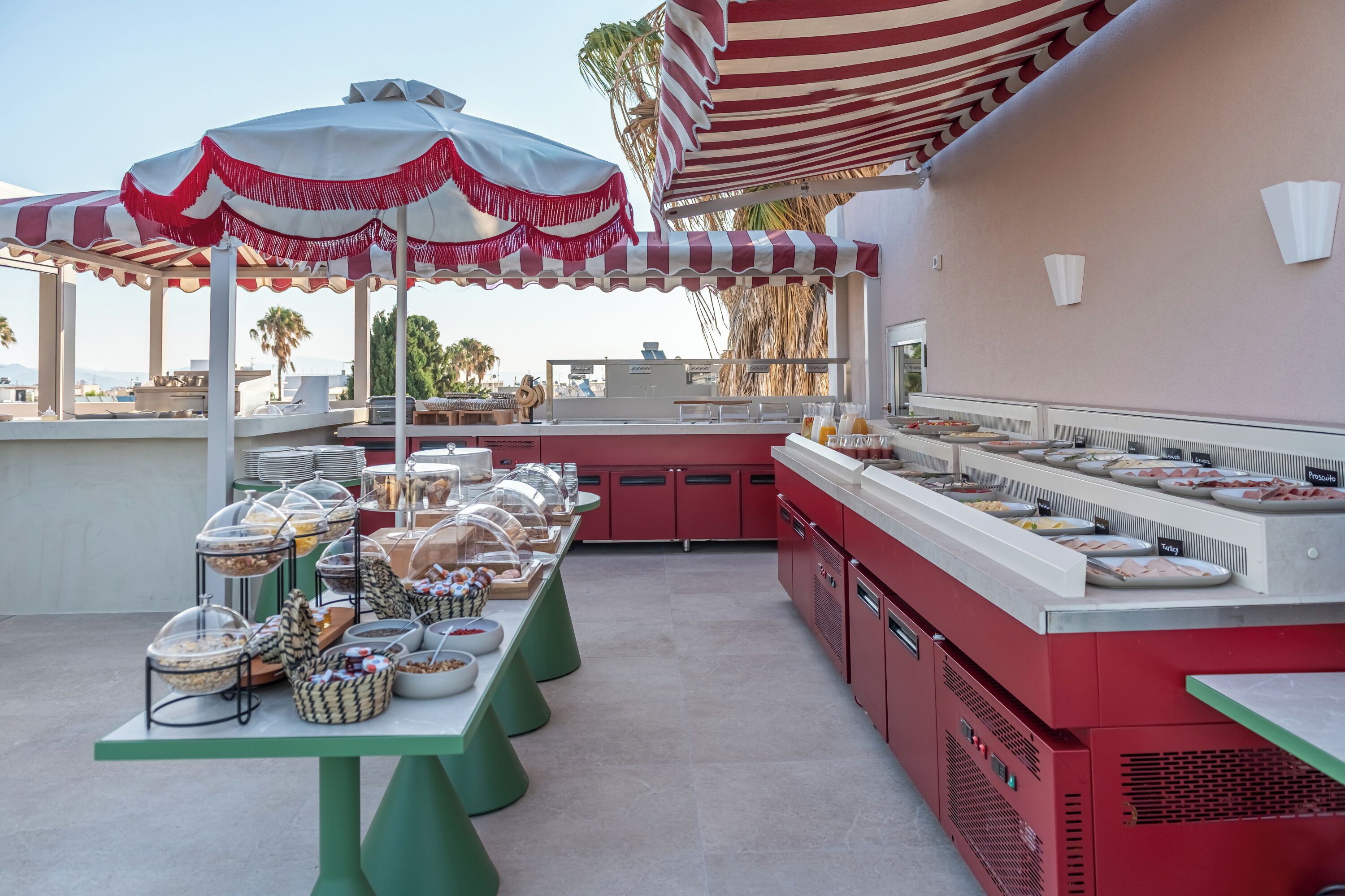 Montaje de buffet al aire libre con diversas opciones de comida, incluyendo carnes y quesos, bajo un toldo a rayas.