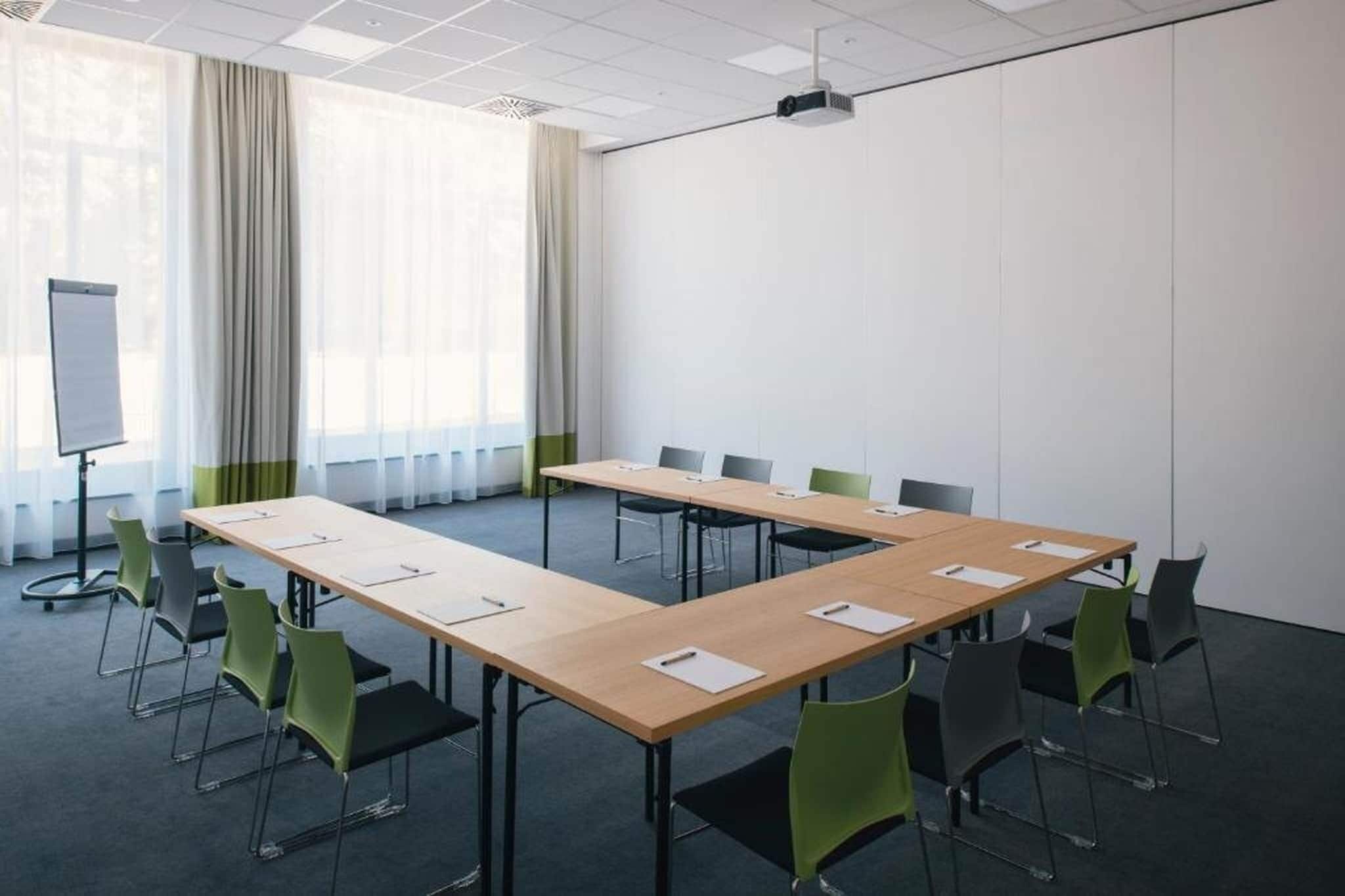 Une salle de conférence avec une longue table, des chaises vertes, un tableau blanc et un projecteur.
