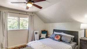 A bedroom with a bed, a ceiling fan, a nightstand, a lamp, a window with curtains, and a radiator. - Walk to Downtown Chico! Tree-Lined Apt w/ Deck (Chico)