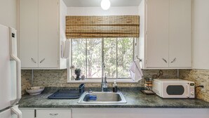 A kitchen with white cabinets, a window with a bamboo blind, a sink, a microwave, and a coffee maker. - Walk to Downtown Chico! Tree-Lined Apt w/ Deck (Chico)