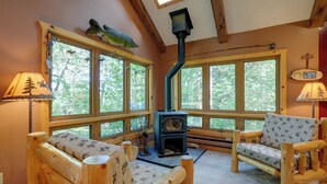 Ein gemütliches Blockhaus-Interieur mit Kaminofen, zwei Holzstühlen und großen Fenstern.