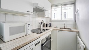 Moderni keittiö, jossa on valkoiset kaapit, sisäänrakennettu mikroaaltouuni, liesi ja astianpesukone.
