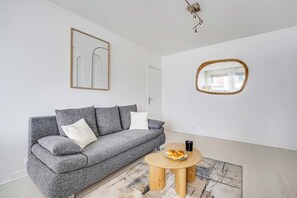 Ein modernes Wohnzimmer mit einem grauen Sofa, einem runden Couchtisch aus Holz, einem gerahmten abstrakten Kunstwerk und einem Spiegel.