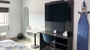 Ein modernes Hotelzimmer mit Fernseher, Schreibtisch mit Stuhl, großem Spiegel und Bügeleisen.