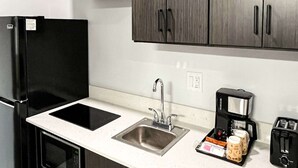 Uma cozinha compacta com geladeira preta, pia, cafeteira e torradeira.