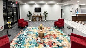 A lobby with a large colorful rug, two red chairs, a wooden coffee table, and a TV mounted on the wall. - 1 King Bed|Non-Smoking,Micfridge (Houston)