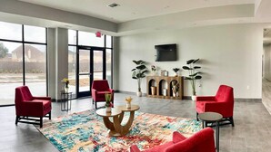 A spacious lobby with large windows, red chairs, a wooden cabinet with plants, and a flat-screen TV on the wall. - 1 King Bed|Non-Smoking,Micfridge (Houston)