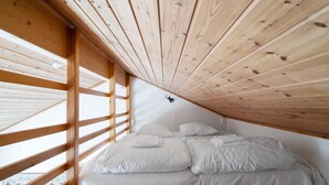 Un dormitorio con techo inclinado, vigas de madera y una cama con ropa de cama blanca.