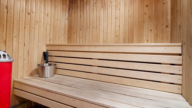 Un banco de madera con un cubo metálico y utensilios, probablemente para una sauna o baño de vapor.