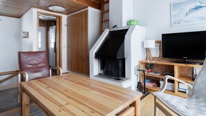 Una habitación con una mesa de madera, una silla roja, una chimenea, un televisor y una estantería.