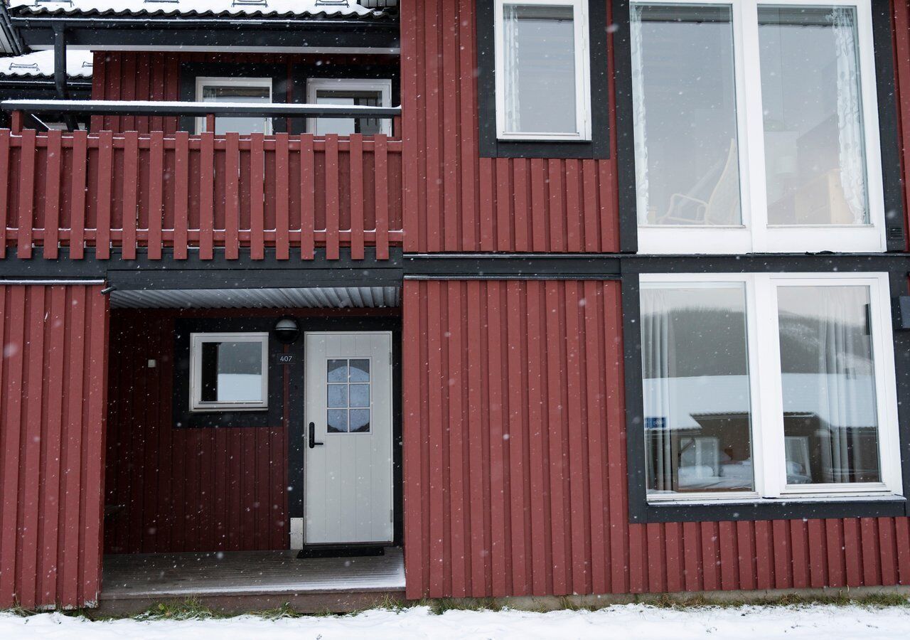 En tvåvåningsbyggnad med en röd fasad, en vit dörr och en balkong.