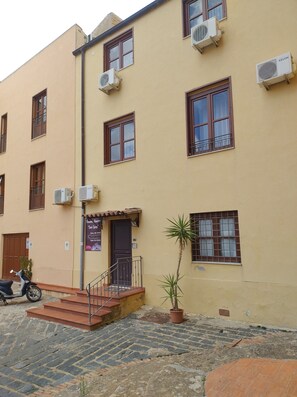 A multi-story building with air conditioning units, a small entrance with steps, and a potted plant. - Monastero Santo Spirito Rooms (Agrigento)