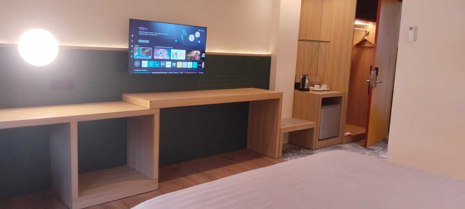 Hotellihuone, jossa on sänky, seinälle asennettu televisio, puinen työpöytä ja vaatekaappi.
