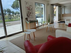 Ein modernes Wohnzimmer mit einem roten Sofa, weißen Sesseln, einem Couchtisch und einem Essbereich mit Tisch und Stühlen.