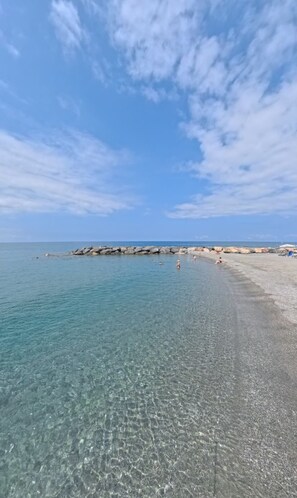 Ein Strand mit klarem Wasser, felsigem Ufer und einigen Personen.