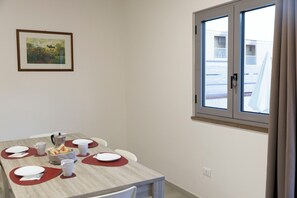 A dining area with a table set for four, a painting on the wall, and a window with a view of buildings. - Residence in Amantea with 2 bedrooms sleeps 6 (Amantea)