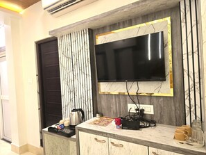 A modern living area with a flat-screen TV mounted on a marble wall, a coffee maker, and a power strip on a marble countertop.