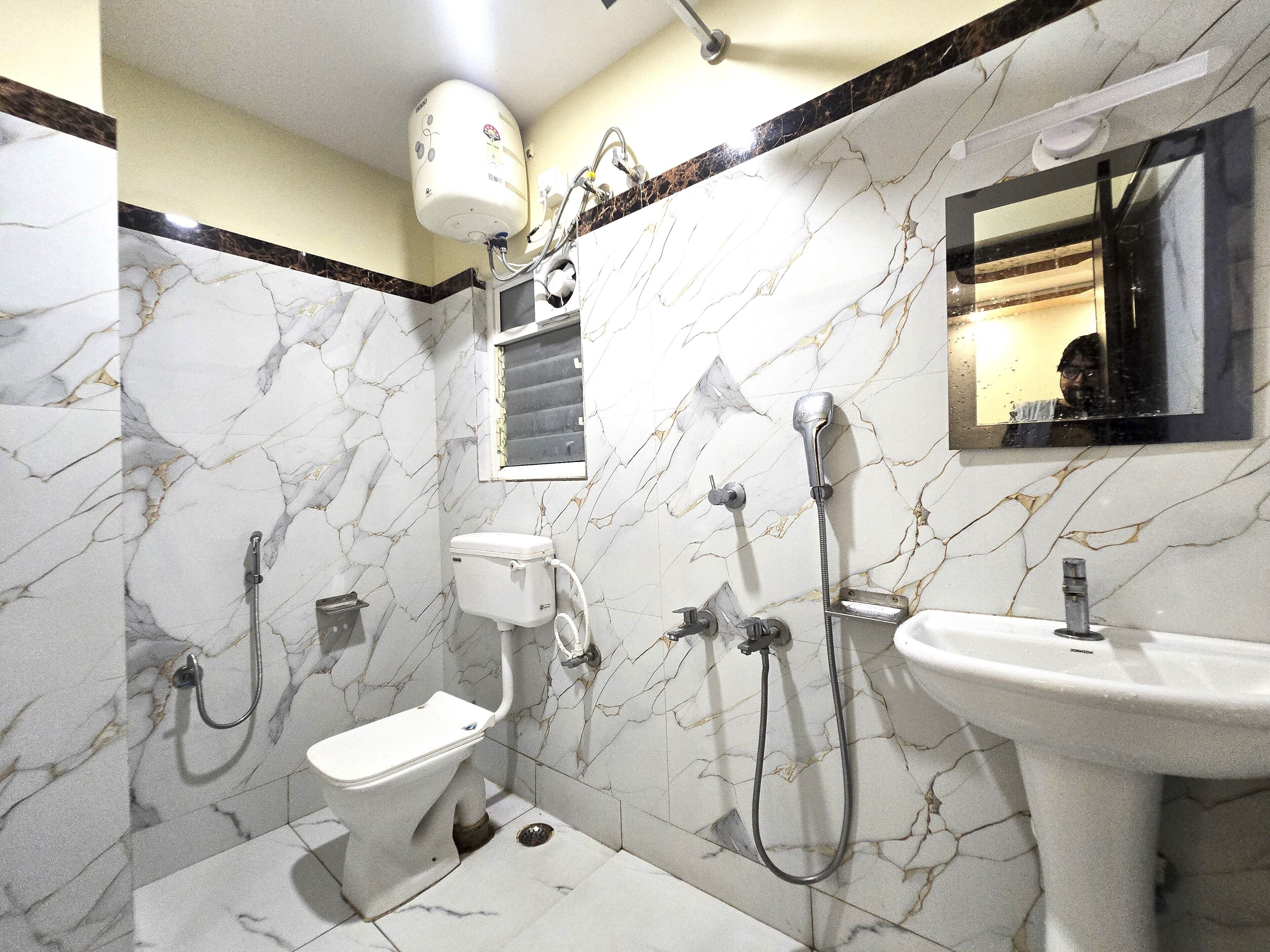 Ein Badezimmer mit Toilette, Dusche und Waschbecken, alles vor einer Marmorwand.