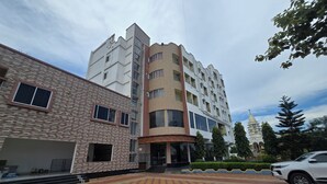 A multi-story building with a mix of brick and modern design elements, a parking area with patterned paving, and a pagoda-like structure in the background.