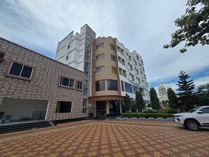 A multi-story building with a mix of brick and modern design elements, a parking area with patterned paving, and a pagoda-like structure in the background.