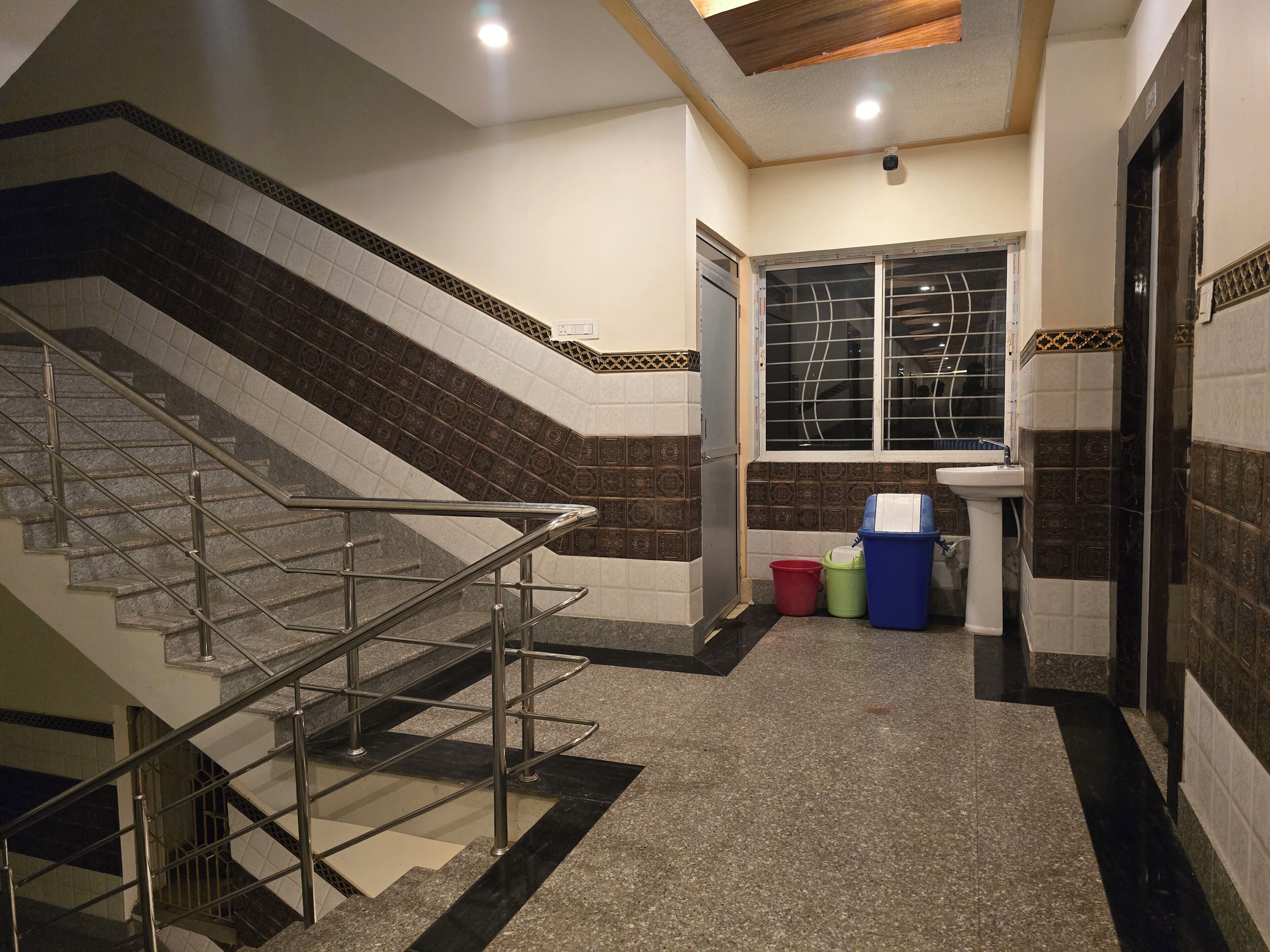 Una escalera con barandillas metálicas, un ventanal con rejas y un lavamanos sobre pedestal.