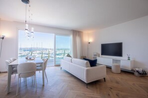 Ein modernes Wohnzimmer mit Essbereich, einer Couch, einem Fernseher und Blick auf einen Yachthafen.